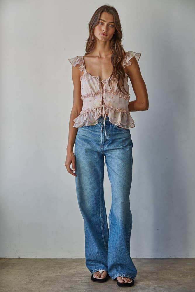 Woman wearing a pink floral blouse and blue jeans against a plain background