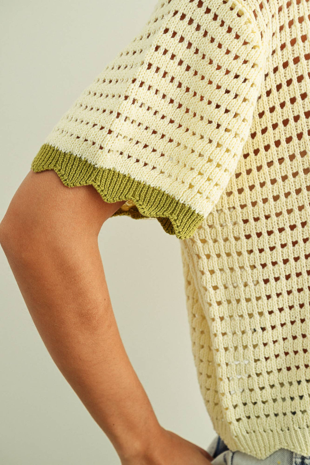 Close-up of a woman wearing a textured beige sweater with green trim on a neutral background