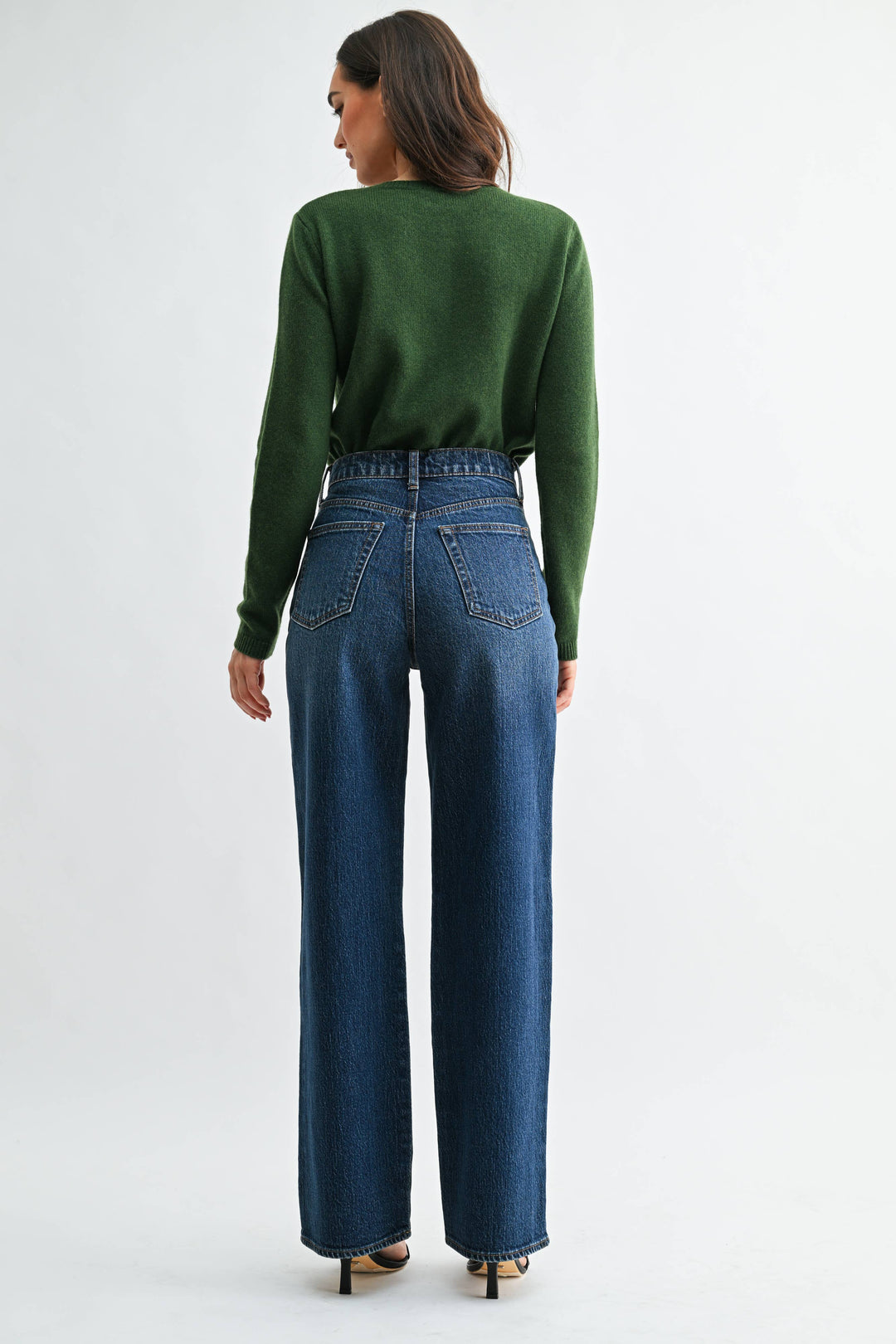 Person wearing a green sweater and dark  blue wide leg jeans on a white background