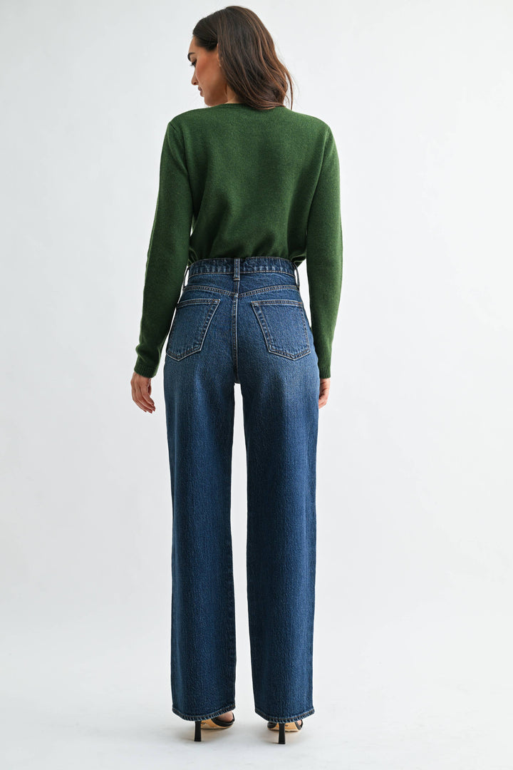 Person wearing a green sweater and dark  blue wide leg jeans on a white background