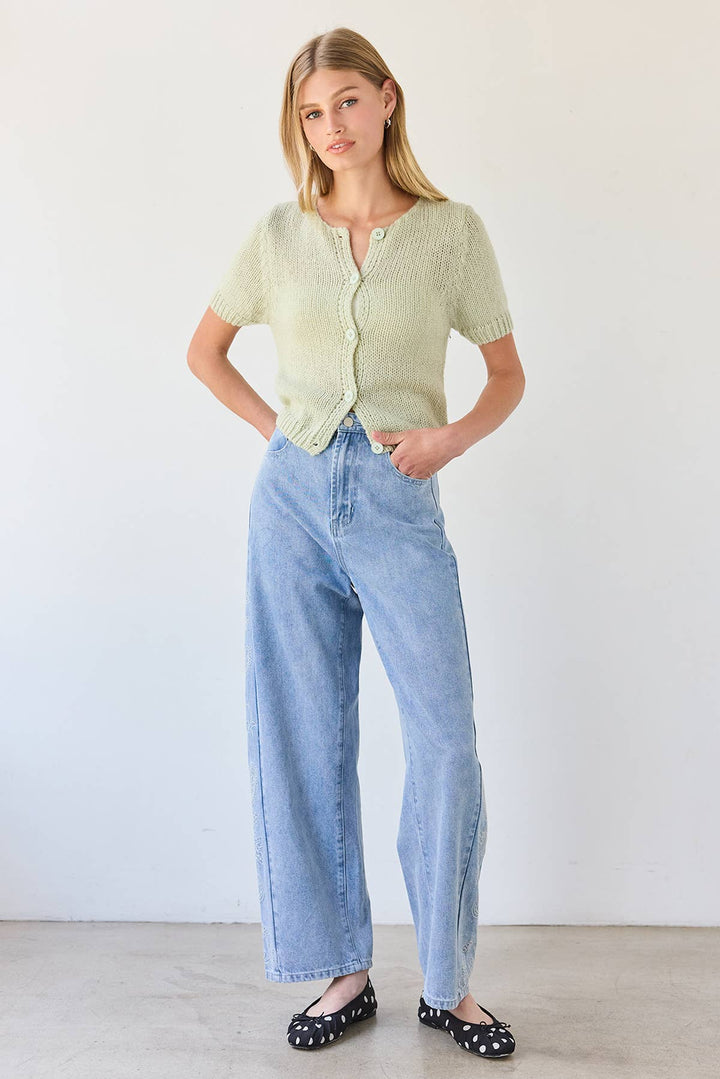 Woman wearing a light green cardigan and blue jeans against a white background