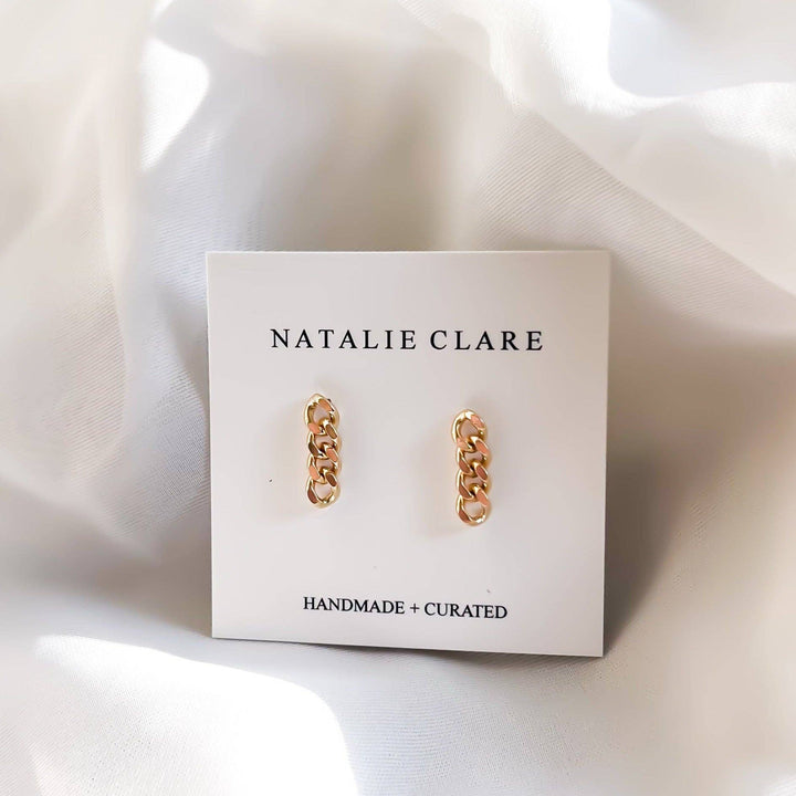 Gold chain earrings on a 'Natalie Clare' branded card with a white fabric background