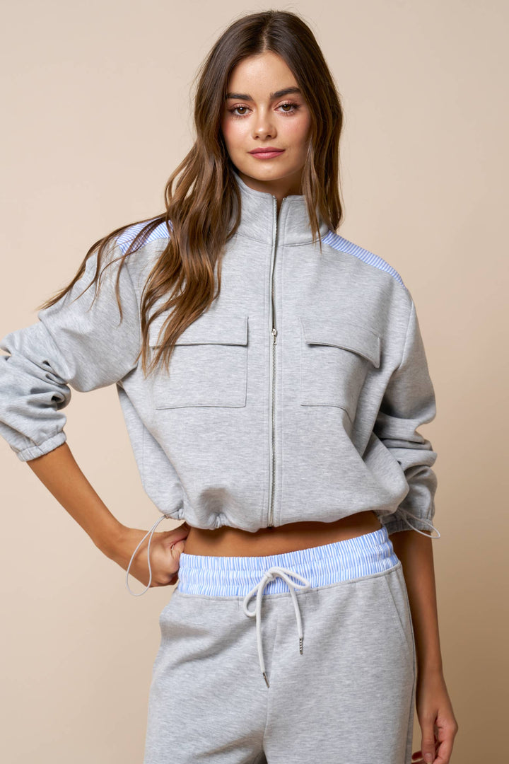 Woman wearing a gray zip-up sweatshirt and sweatpants on a beige background