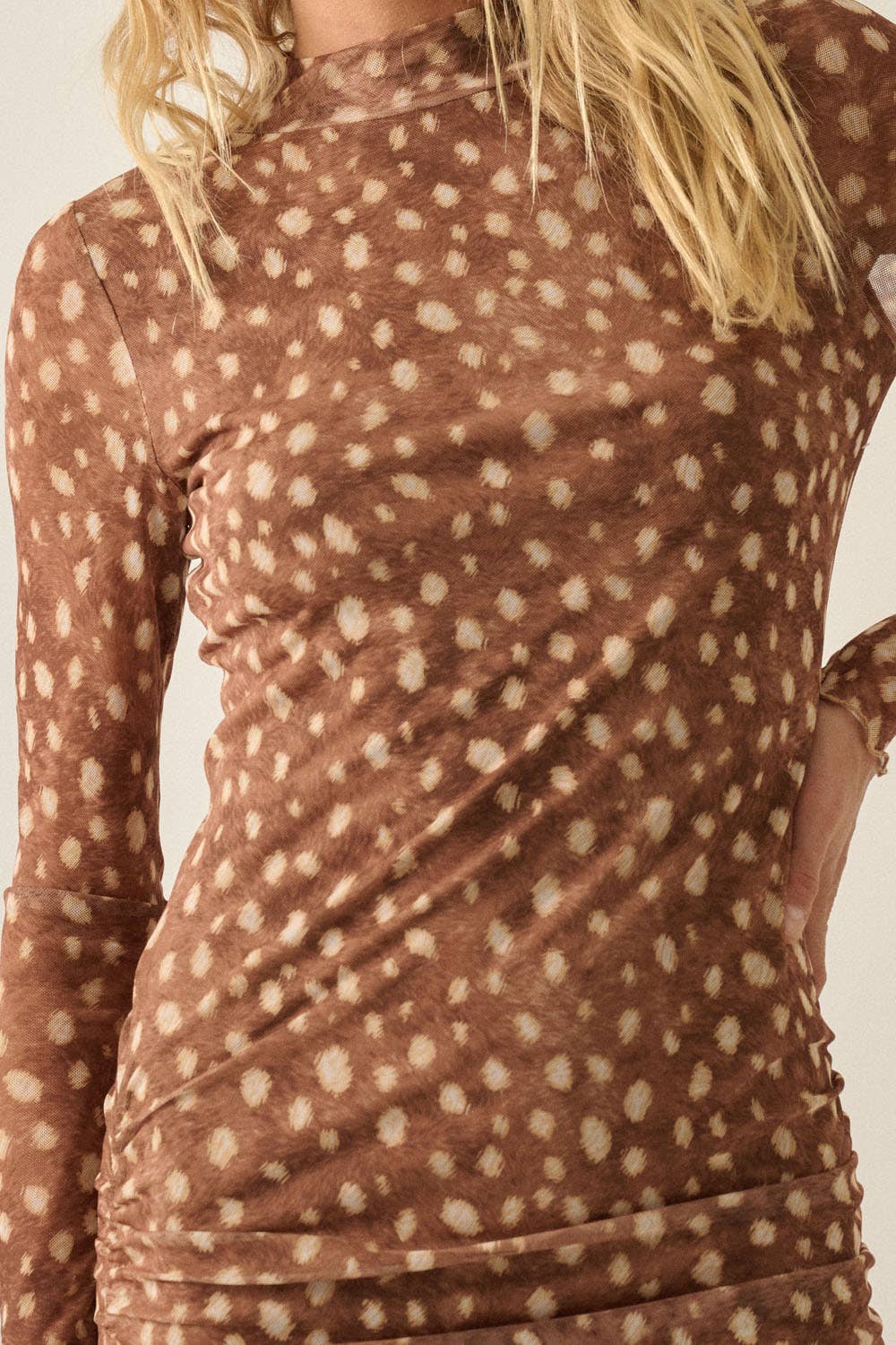 A close-up of a woman wearing a brown long-sleeve mock-neck top with a beige bambi print pattern, showing the ruched side details and her blonde hair.