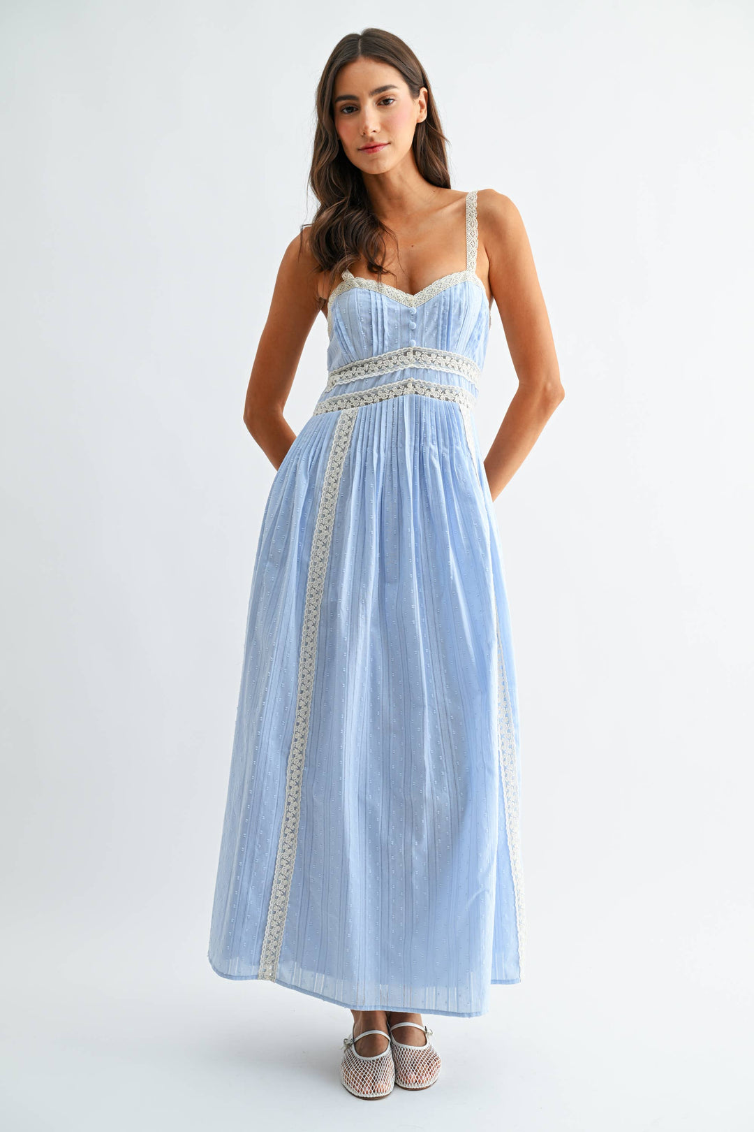 Woman wearing a light blue sleeveless dress with white embellishments and on a white background