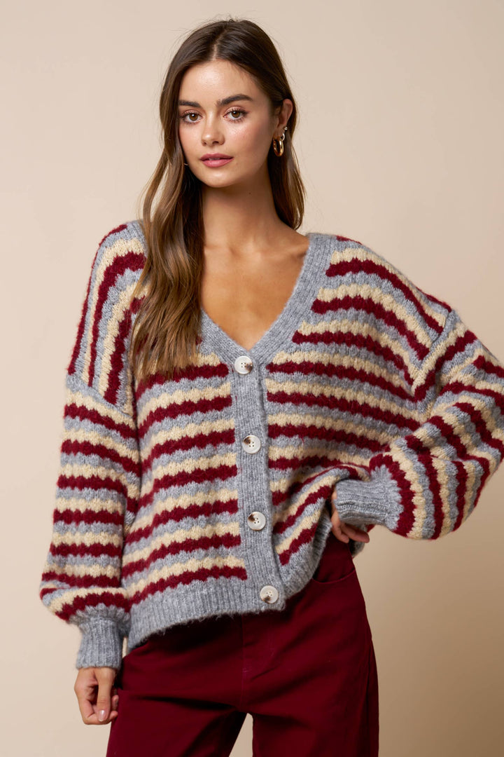 Woman wearing a burgundy and gray striped cardigan sweater with a neutral background