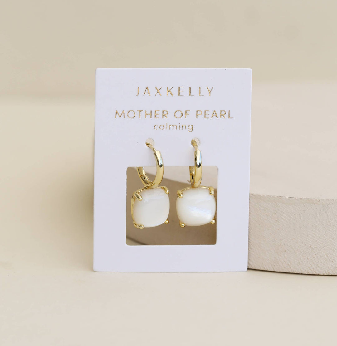 Jaxkelly drop huggie mother of pearl earrings on a display card with a beige background