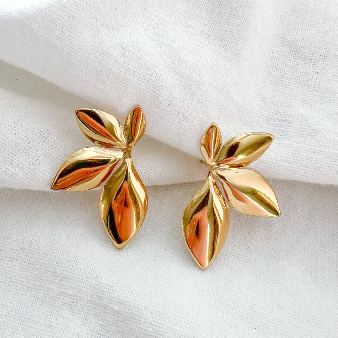 Gold leaf-shaped earrings on a white fabric background