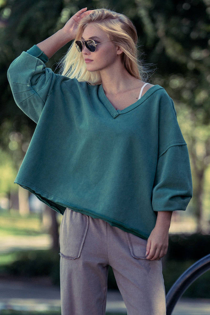 Woman wearing a teal v-neck sweatshirt and sunglasses outdoors
