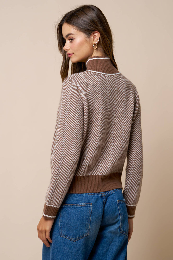 Woman wearing a brown sweater with a high collar and blue jeans on a beige background