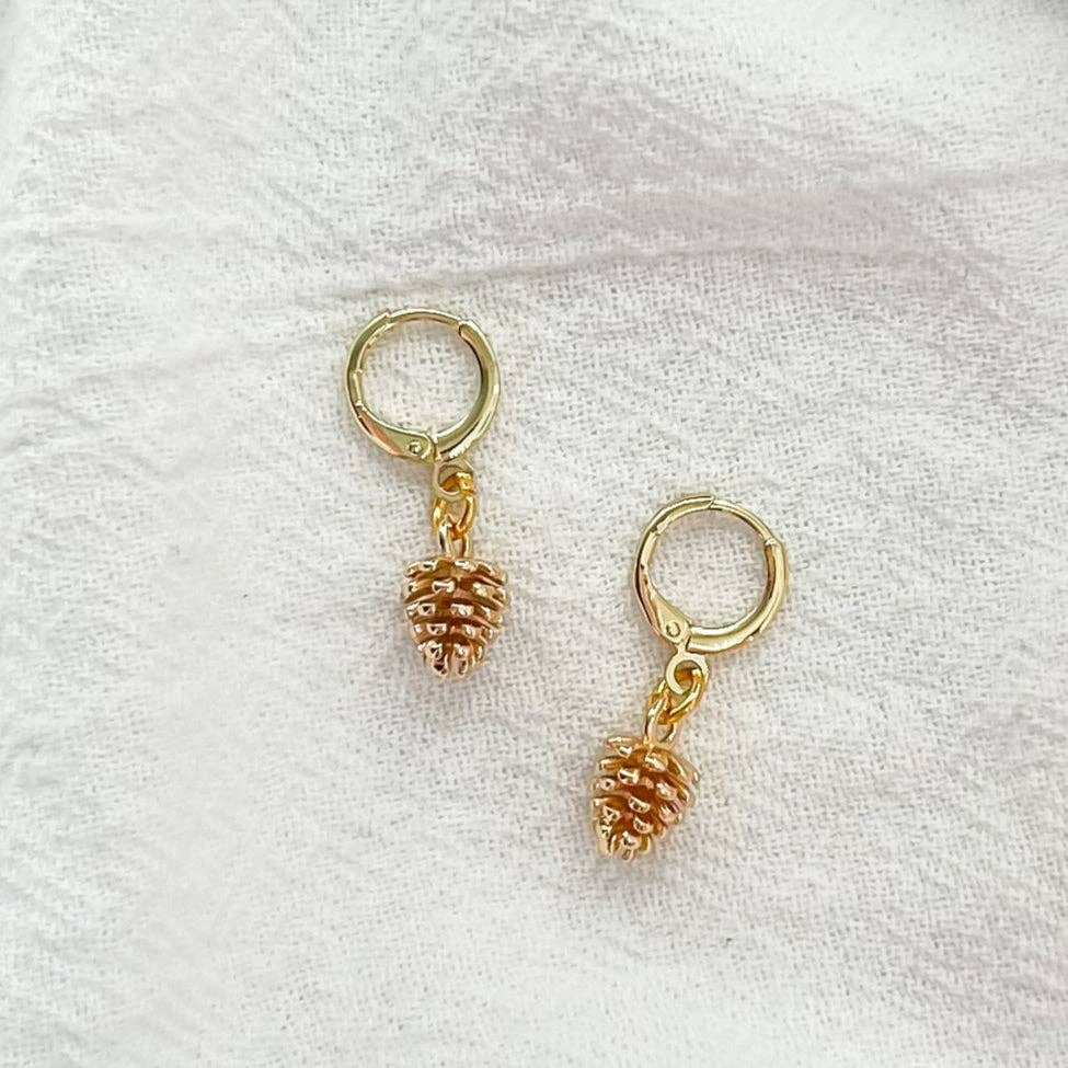 Gold drop huggie pinecone earrings on a white fabric background