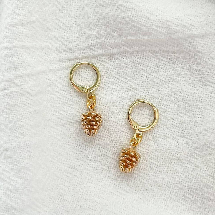 Gold drop huggie pinecone earrings on a white fabric background