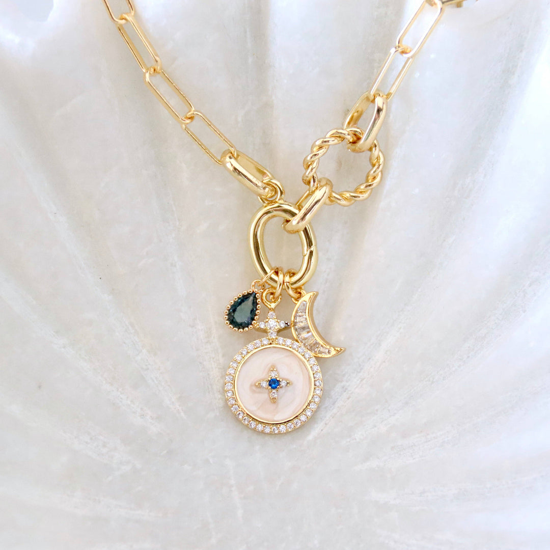 Gold necklace with a circular pendant and moon charm on a white fabric background