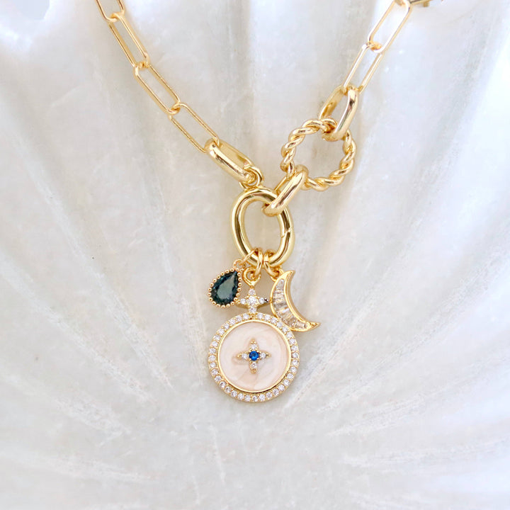 Gold necklace with a circular pendant and moon charm on a white fabric background