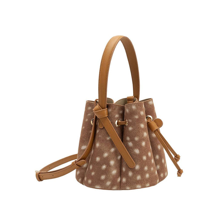 Brown polka dot bucket bag with tan leather straps on a white background