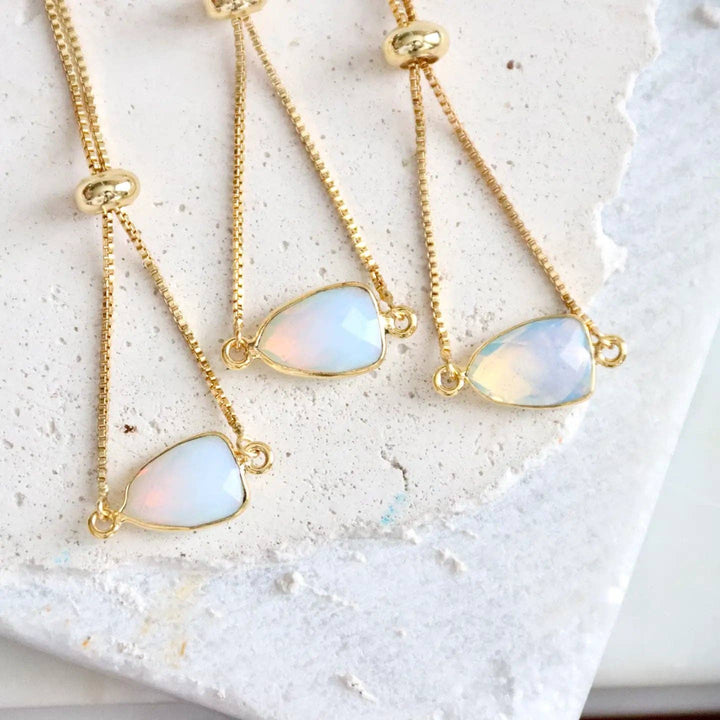 Three gold bracelets with opalite stones on a textured white surface