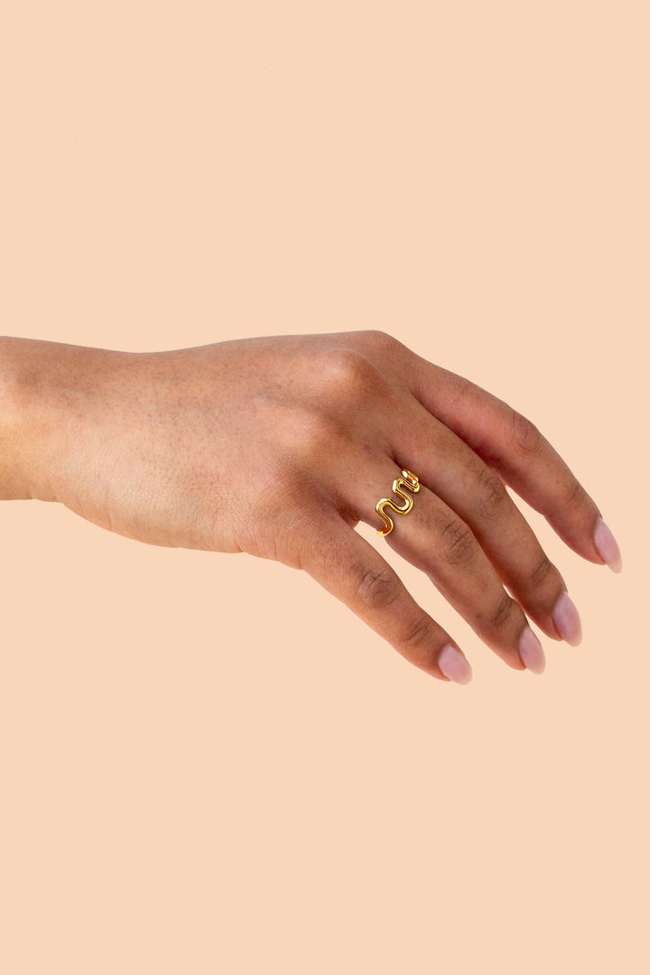 Hand wearing a gold ring on a beige background