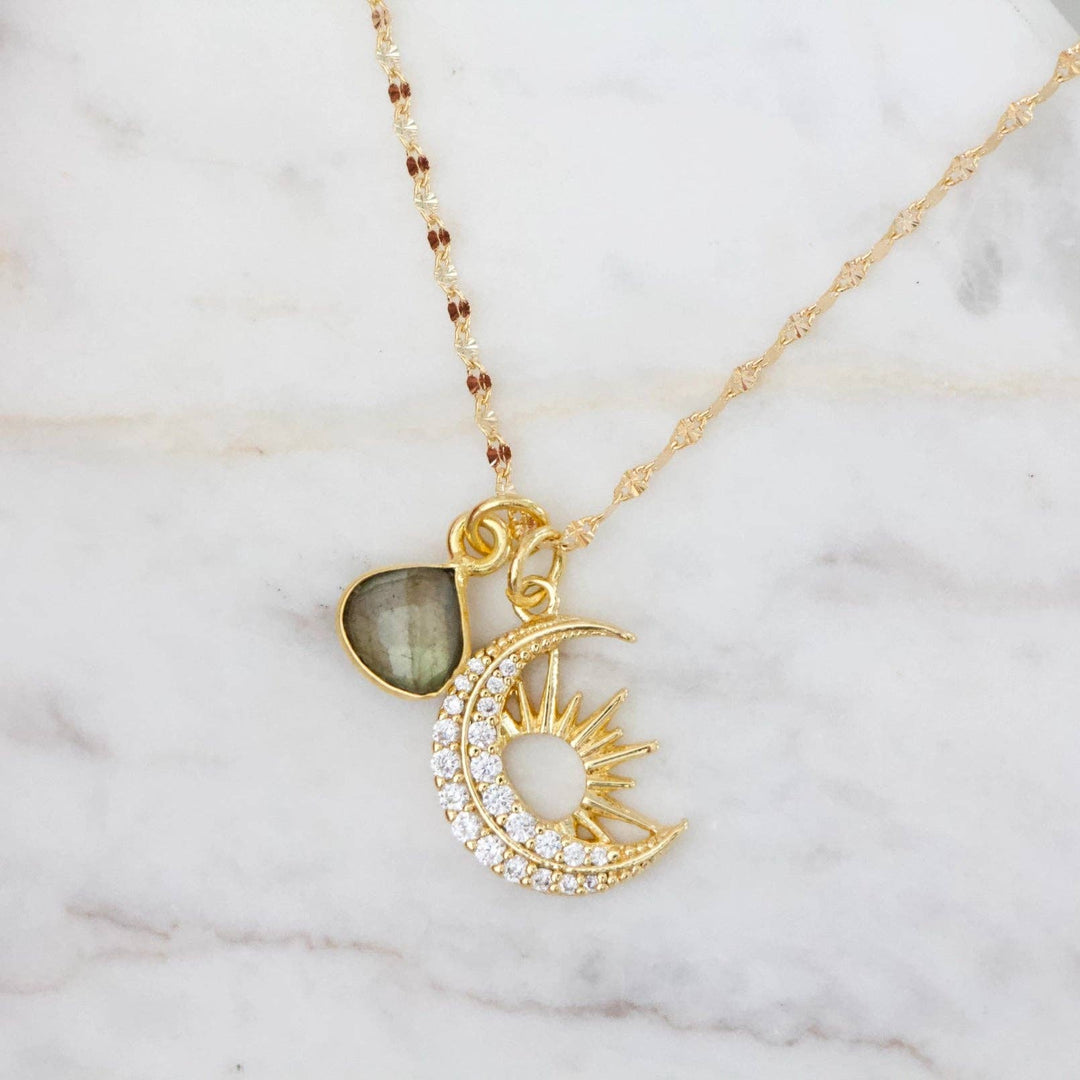 Gold necklace with moon and sun and labradorite pendant on a marble surface