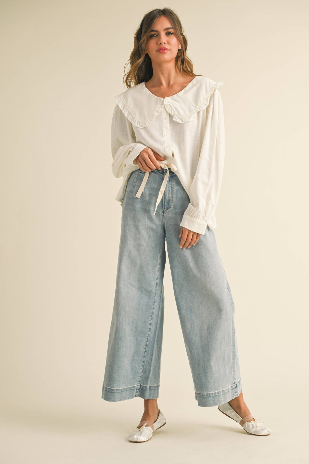 Woman wearing a light wash blue wide leg light weight jeans with drawstring waist 