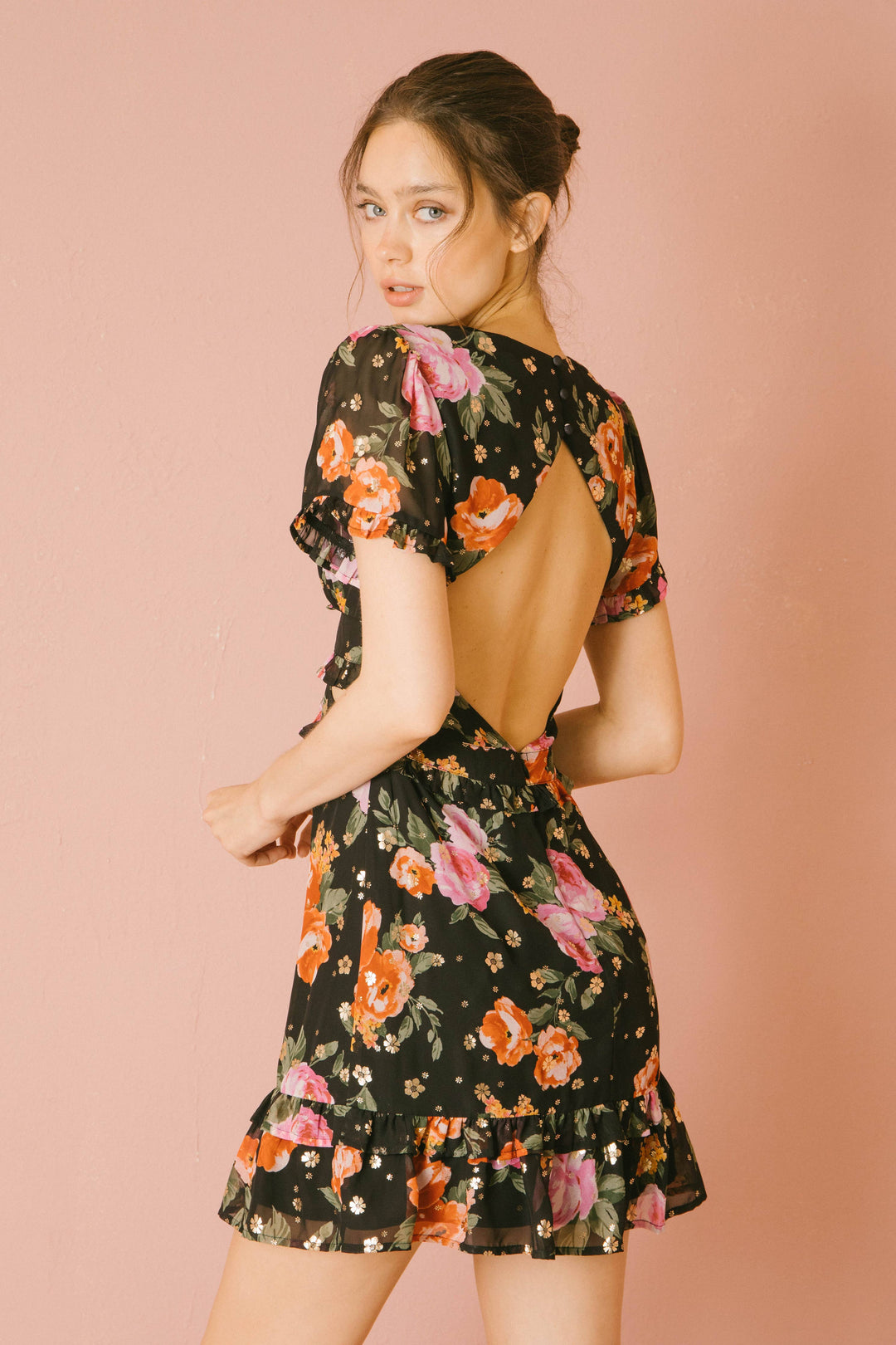 Woman wearing a black floral mini dress with an open back on a pink background