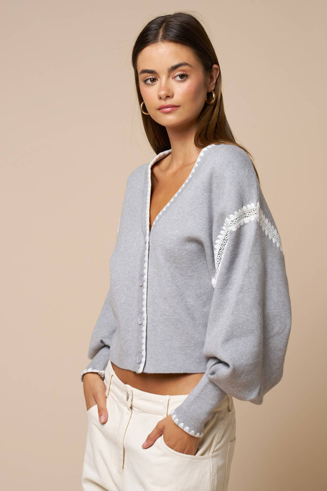 Woman wearing a light gray cardigan with lace trim on a beige background