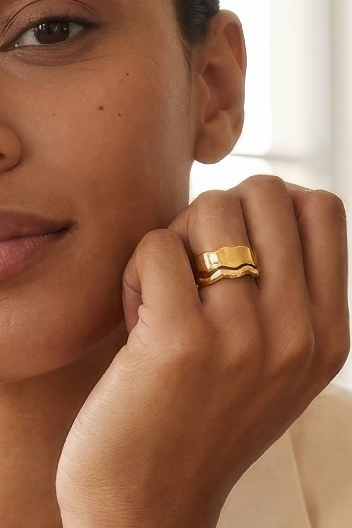 Close-up of a woman's hand wearing a gold stacking ring with a blurred background