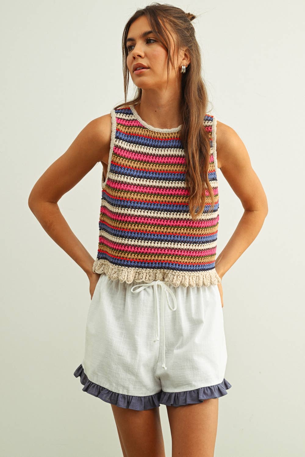 Woman wearing a colorful striped crochet knit tank top and white shorts on a plain background