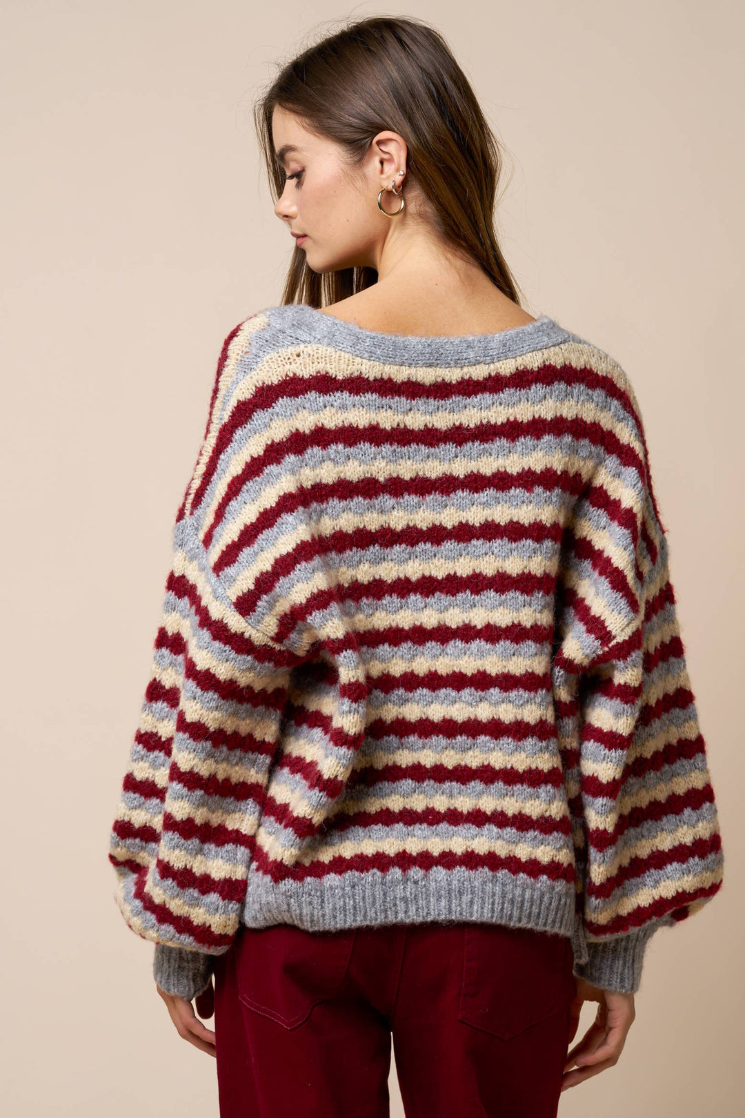 Woman wearing a striped sweater with drop shoulder and oversized fit a neutral background