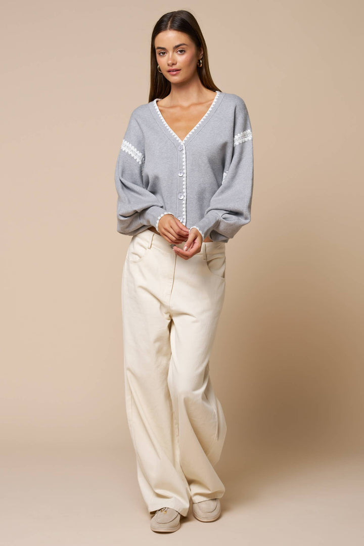 Woman wearing a light gray with white trim and beige pants against a beige background