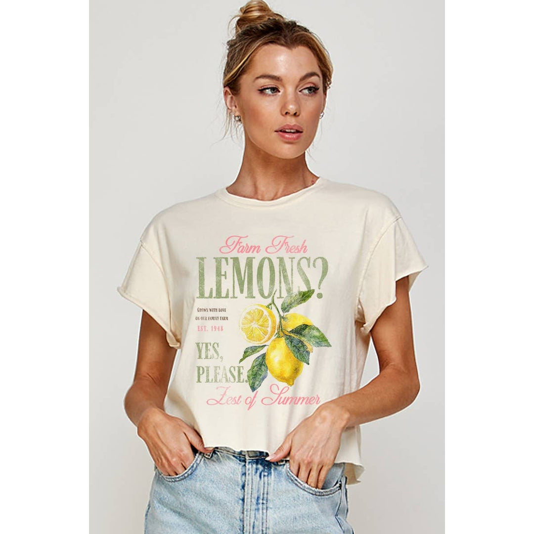 Woman wearing a cream cropped  t-shirt with lemon graphic and text on a plain background