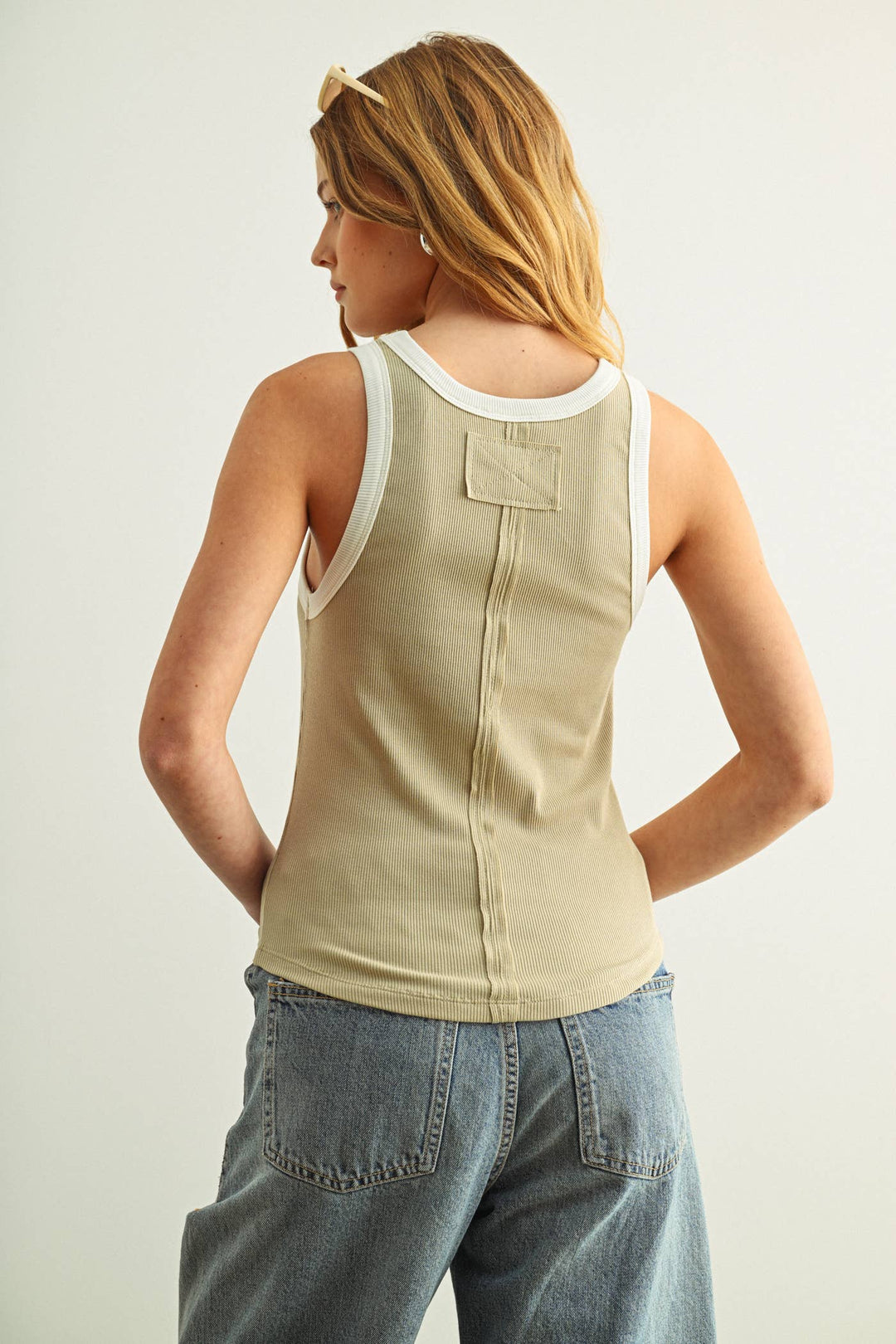 Woman wearing a beige tank top with white trim and blue jeans on a plain background