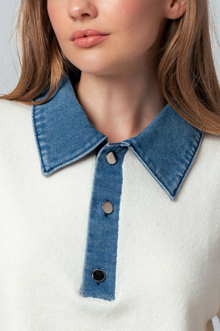 Close-up of a person wearing a white sweater with a blue denim collar and buttons.