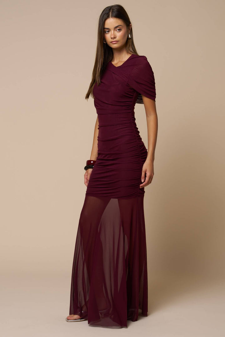 Woman wearing a burgundy dress with sheer overlay on a beige background