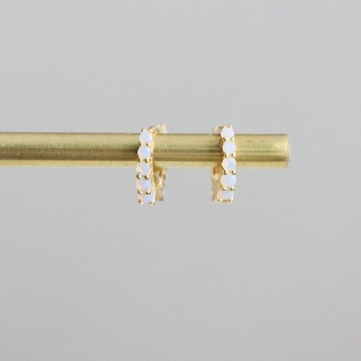 Gold hoop earrings with small opalite stones on a gray background