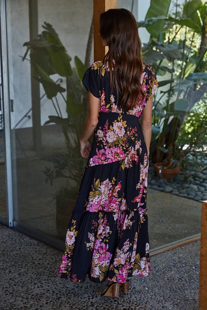 Woman in a black floral midi dress standing in an outdoor setting with plants.