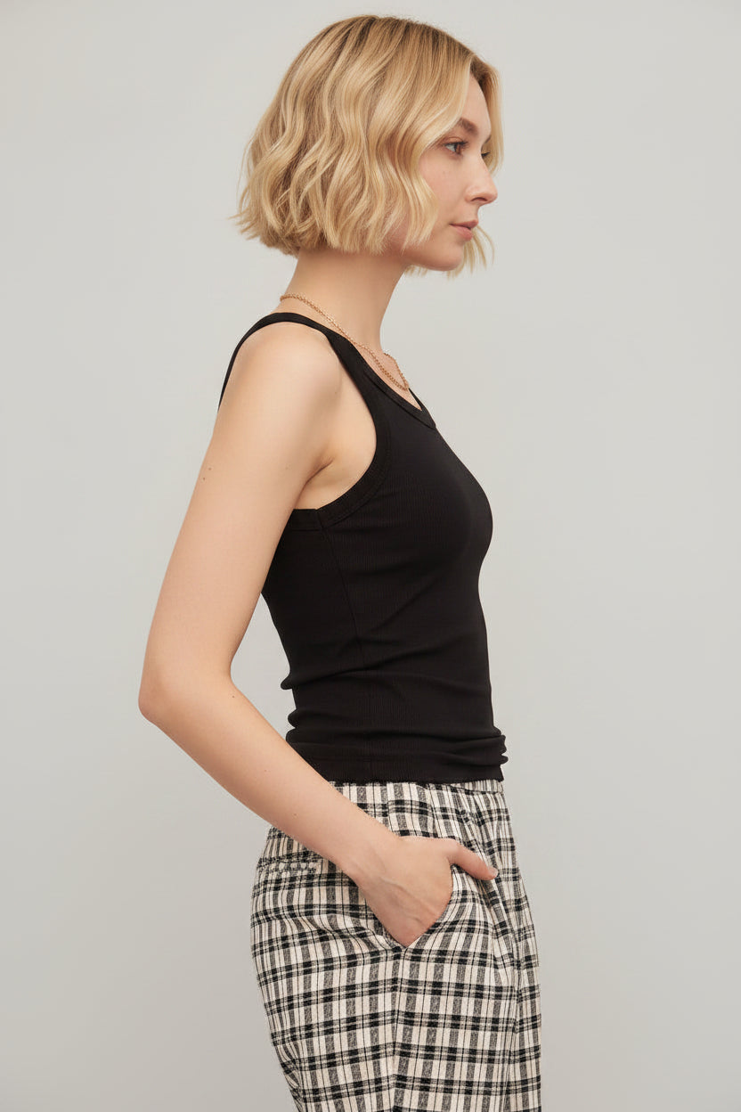 Woman wearing a white tank top and plaid pants against a plain background