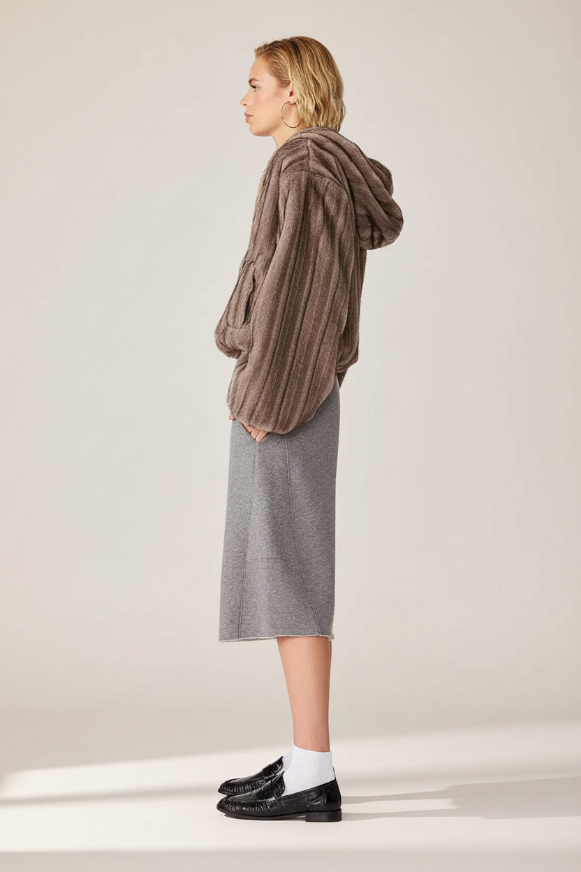 A model shown from the side profile wearing a brown ribbed knit hooded sweater, a gray midi skirt, white socks, and black loafers against a plain white background.