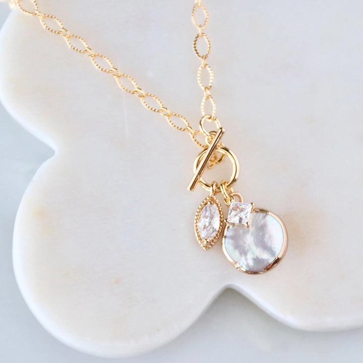Gold necklace with a fresh water pearl charm and cz charms on a white dish