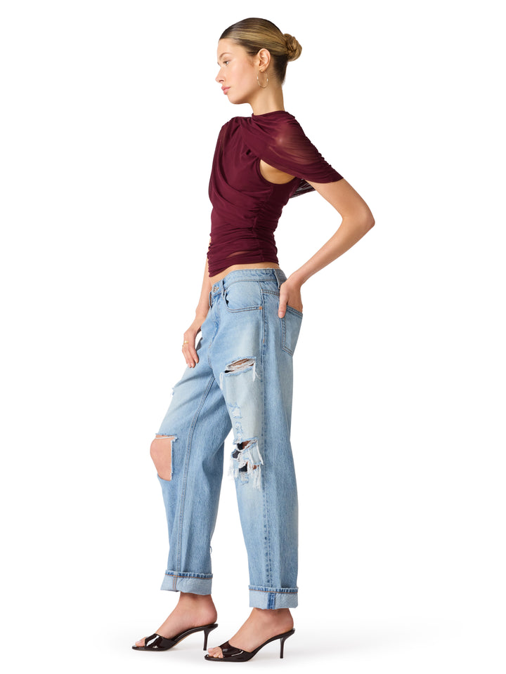 A woman modeling a maroon short-sleeve mesh top and light-wash distressed jeans with rolled cuffs, paired with black heeled sandals, against a plain white background.