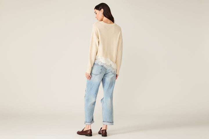 A woman shown from the back wearing a cream knit sweater with lace trim, light-wash blue jeans with lace detailing at the back hem, and dark brown loafers, against a plain white background.