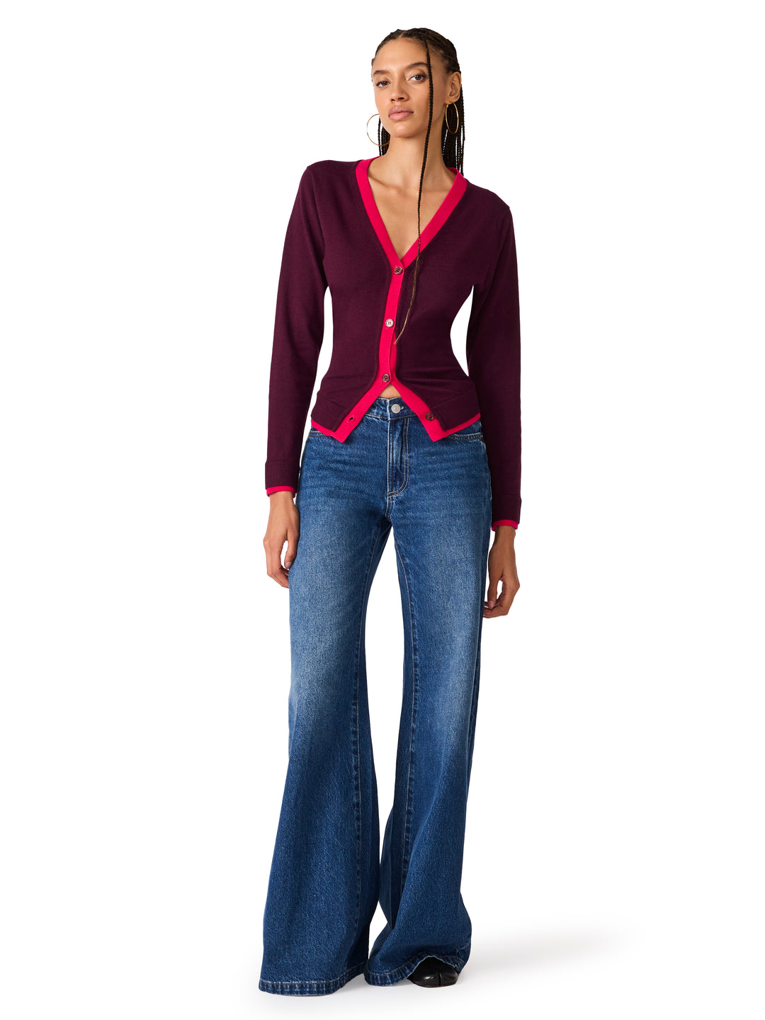 A model wearing a dark purple long-sleeve cardigan with bright pink trim and blue wide-leg jeans, standing against a plain white background.