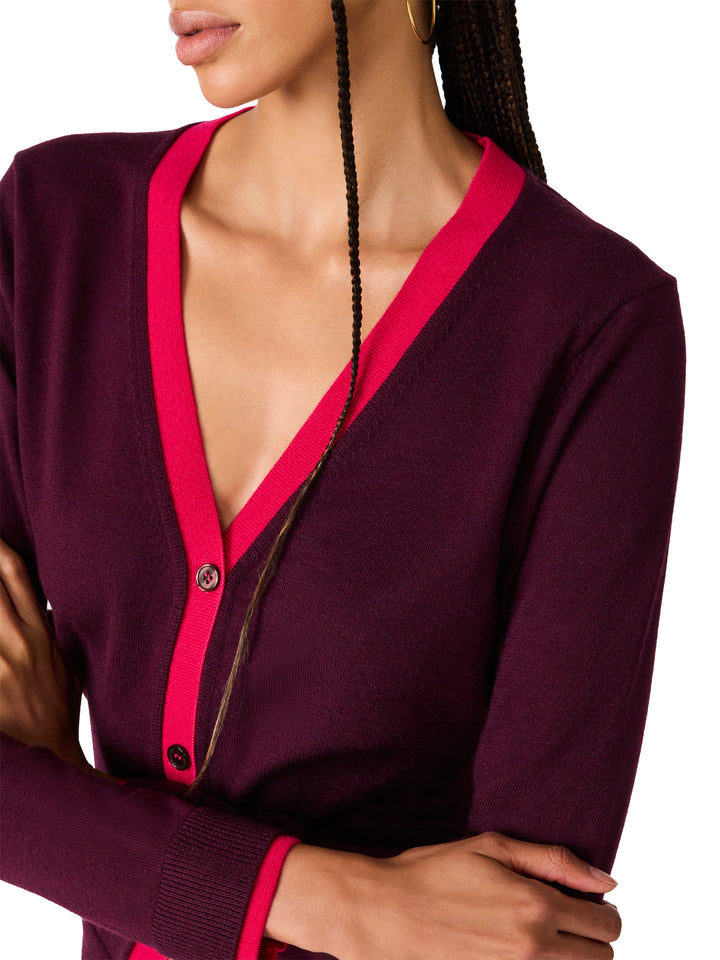 A close-up of a woman wearing a long-sleeve cardigan in deep plum purple with bright pink trim along the V-neck and button placket.