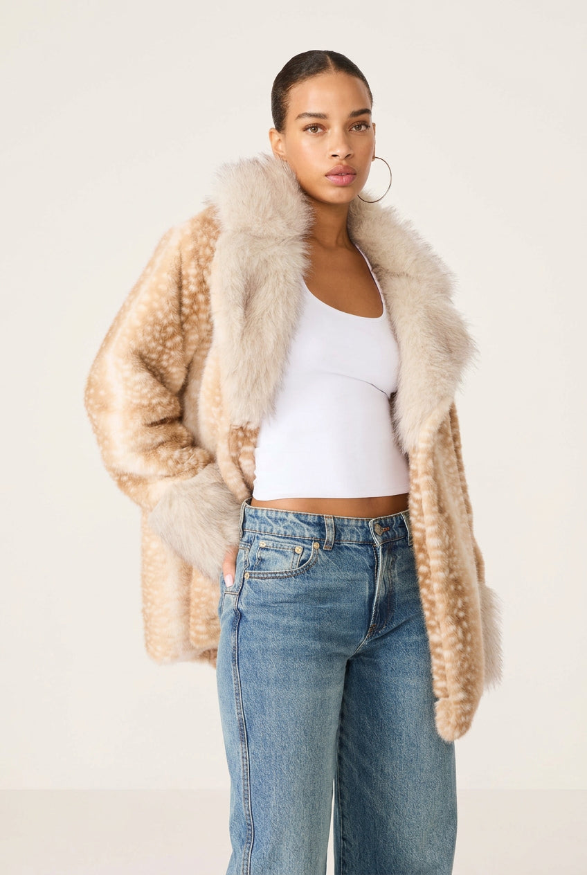 A model wearing a beige faux fur jacket with white spots, a white ribbed tank top, and blue jeans, photographed against a solid white background.