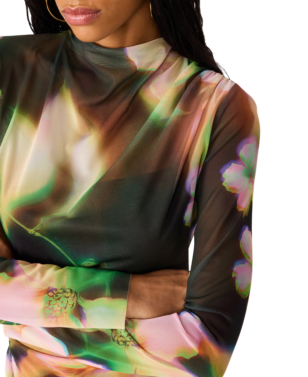 A close-up of a model wearing a sheer, long-sleeve mock-neck dress with an abstract, iridescent floral print in shades of green, pink, and brown against a white background.