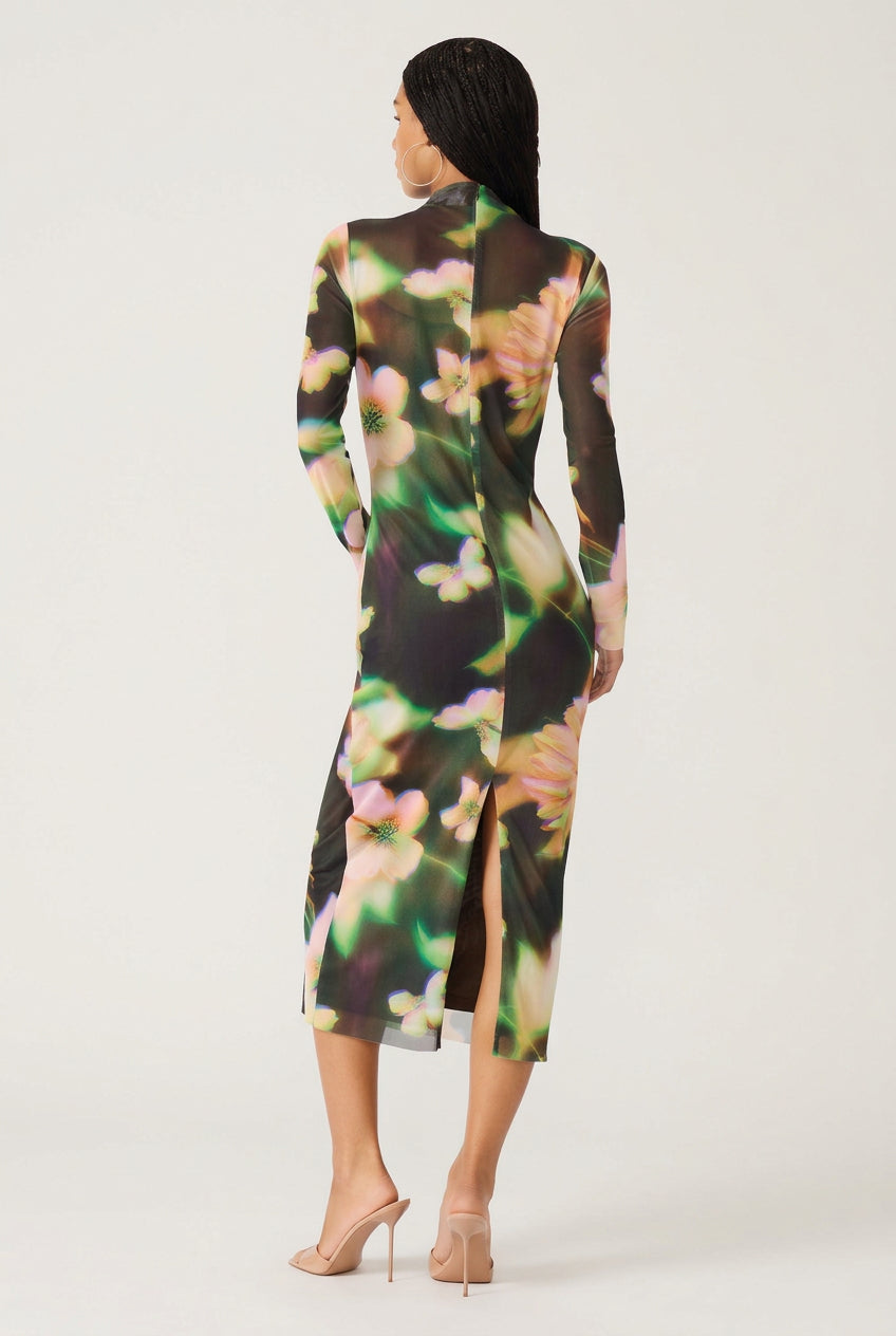 A woman shown from the back wearing a long-sleeve midi dress with a black base and a vibrant, painterly floral pattern in green, pink, and yellow. She is wearing nude high-heeled sandals against a plain white background.