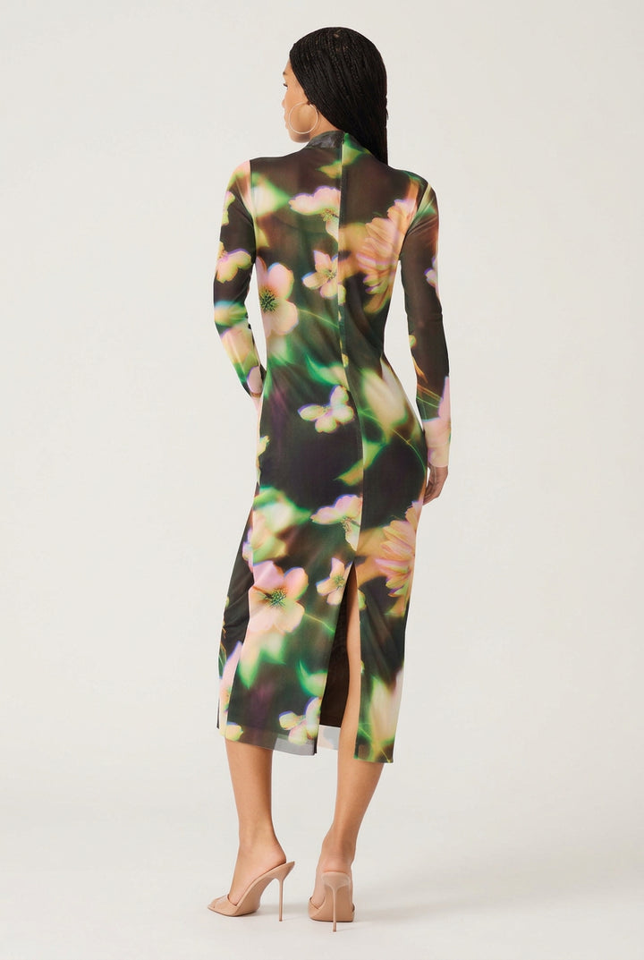 A woman shown from the back wearing a long-sleeve midi dress with a black base and a vibrant, painterly floral pattern in green, pink, and yellow. She is wearing nude high-heeled sandals against a plain white background.