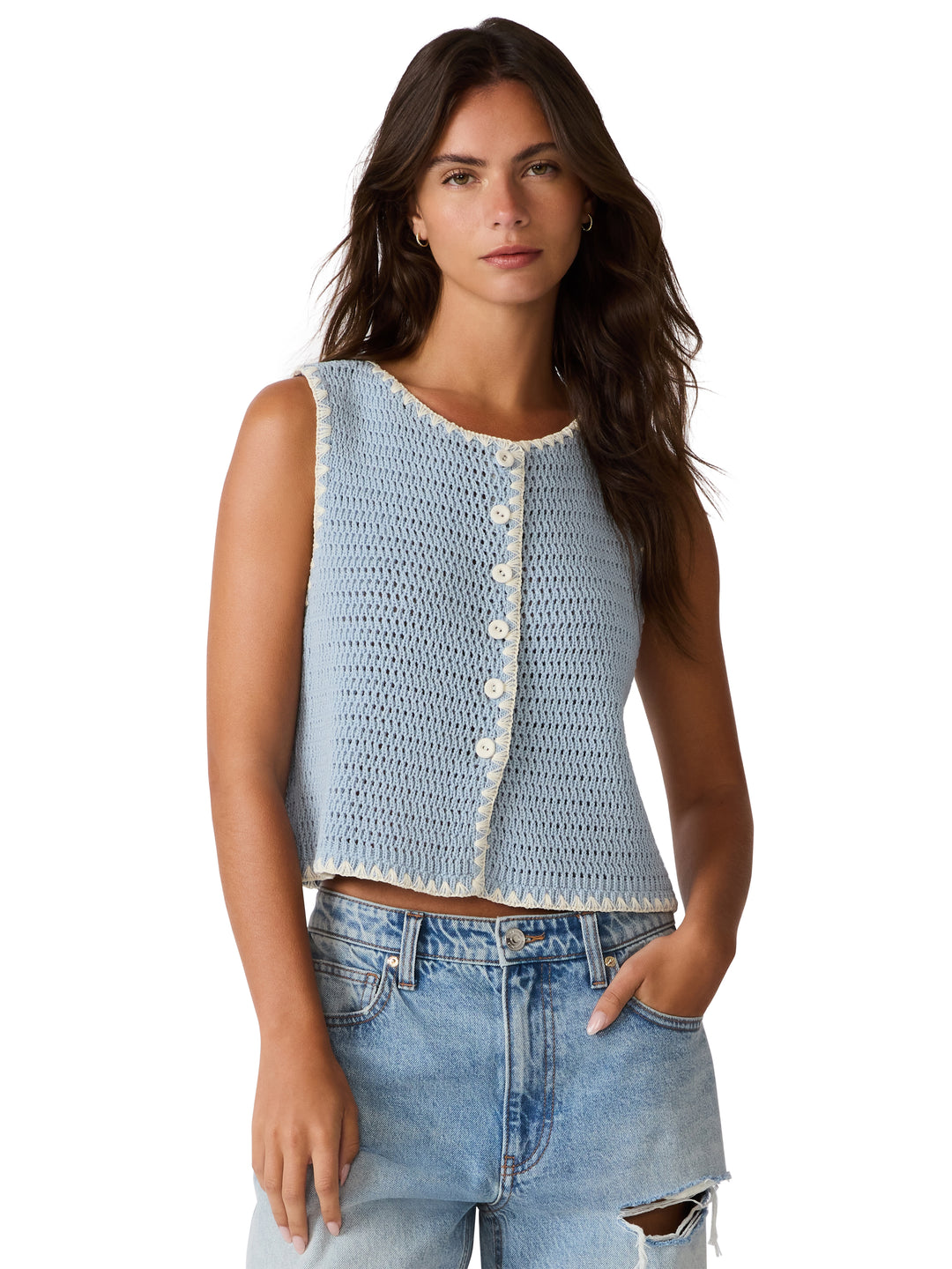 Woman wearing a light blue crochet top with button details and ripped jeans on a white background