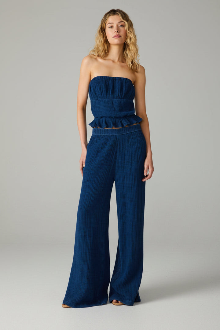 Woman wearing a blue strapless peplum top and matching wide leg pants on a white background