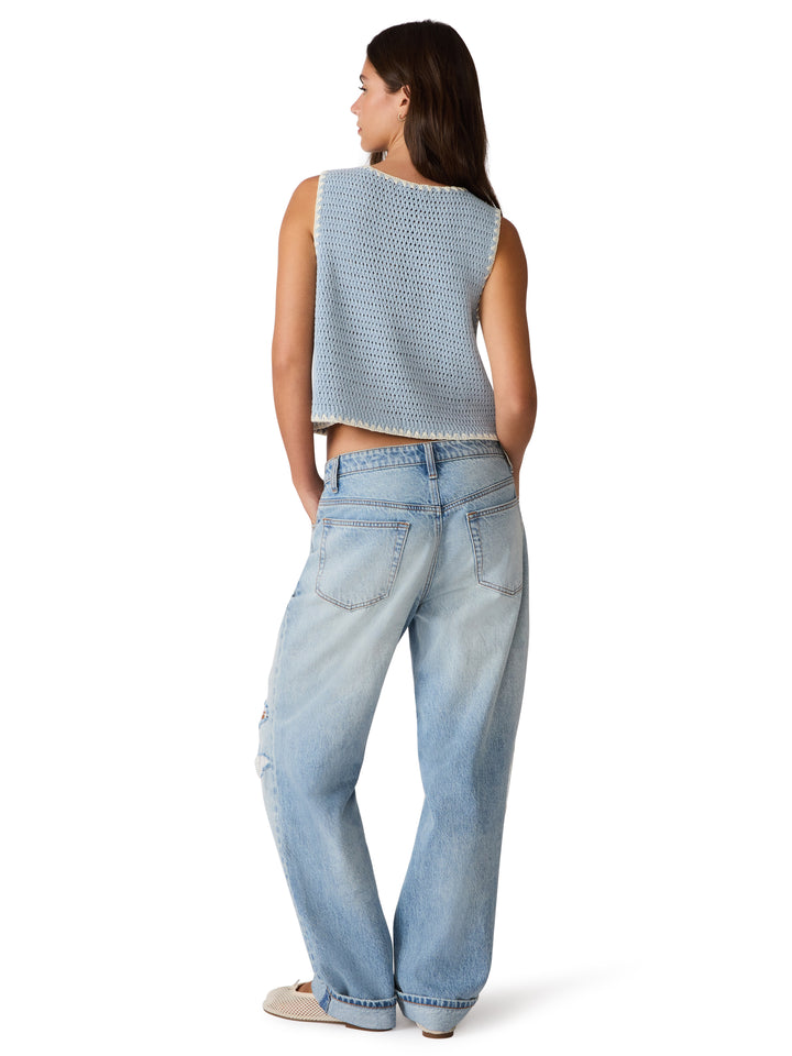 Woman wearing a light blue crochet sleeveless top and jeans on a white background