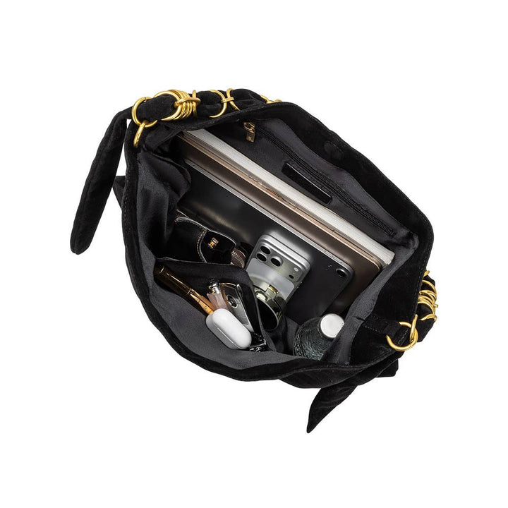 Black suede shoulder bag with gold-tone hardware and a black-and-white checkered strap, shown open to reveal its interior compartments filled with a laptop, wallet, and accessories, on a solid white background.